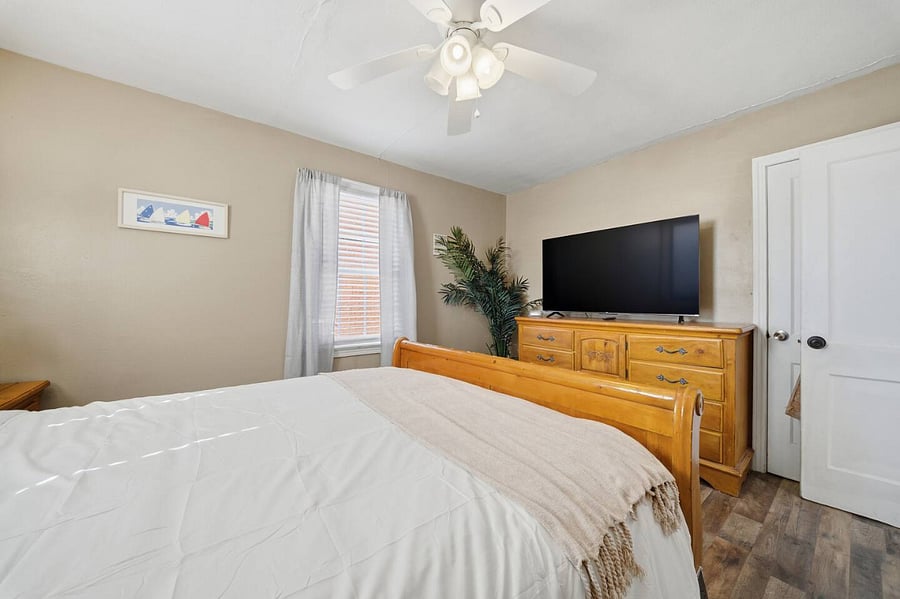 Spacious bedroom featuring a comfortable bed, large dresser, and flat-screen TV for relaxing nights in. Soft neutral tones and a ceiling fan add to the cozy, restful atmosphere.