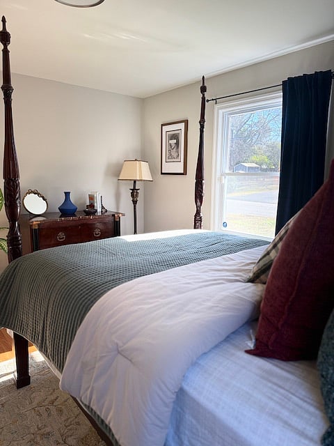 Another angle of the bedroom that has the canopy bed. Clean & nice linens.   A bowl to put your jewelry in. The mid century chest locks.   The ornate brass lamp can be used for extra or dim lighting instead of the ceiling light.  This bedroom has two windows. One this side, it faces the front of the house. The neighbor house that it is  facing is far away. She has a beautiful well kept house.   A full large closet  and a real plant.  