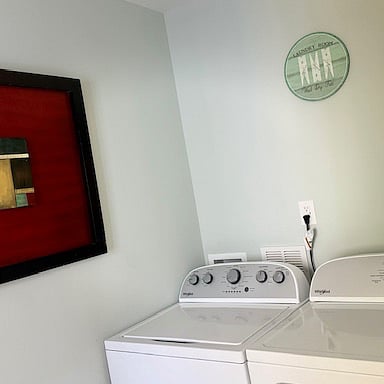 NEW washer and dryer with multiple cycles. Laundry detergent in the bottom of the kitchen cabinet. Laundry hamper for dirty clothes and towels.   There is a door in this area that goes out to the back yard. The trash bins are located there. Beautiful serene backyard and nice trees. 