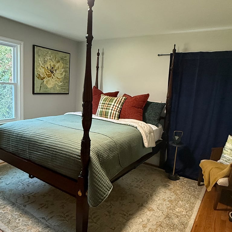 Another view of the Queen Bed. Henkle Harris Canopy bed. new mattress. new box springs.  Black out curtains on both side of the windows.  Comfortable Mid Century chair with throw, plant (no need to water), and games.