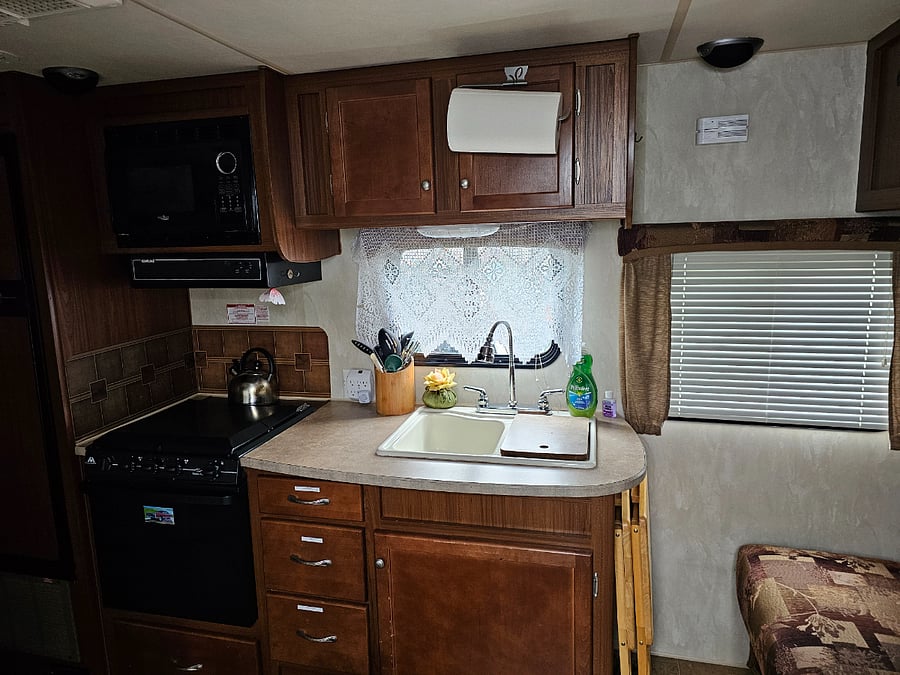 # burner gas stove and oven. Microwave, Double Sink, Cooking Utensils, silverware, cups, plates, dish towels, and garbage bags.