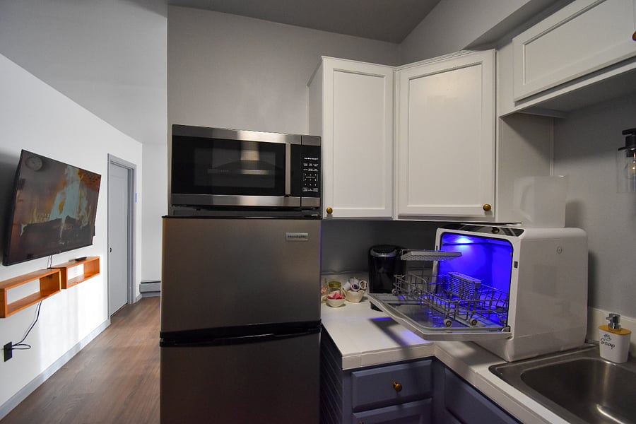 A bright kitchen setup with a large sink, convenient countertop dishwasher, fridge, and microwave. Enjoy fresh coffee from the Keurig or electric kettle, with supplies ready for your morning start.