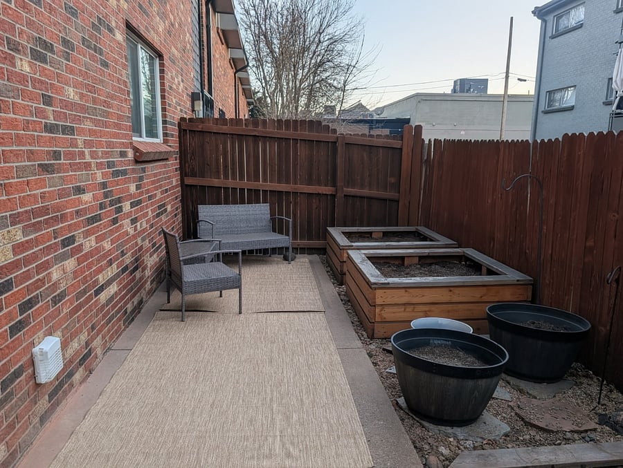 Private fenced in back patio with garden boxes and some perennial green onion and flowers.  The photo looks a little glum right now in the winter but this photo is the most up to date as of Feb 2026. Blue seat cushions are in the garden bench to protect from weather. 