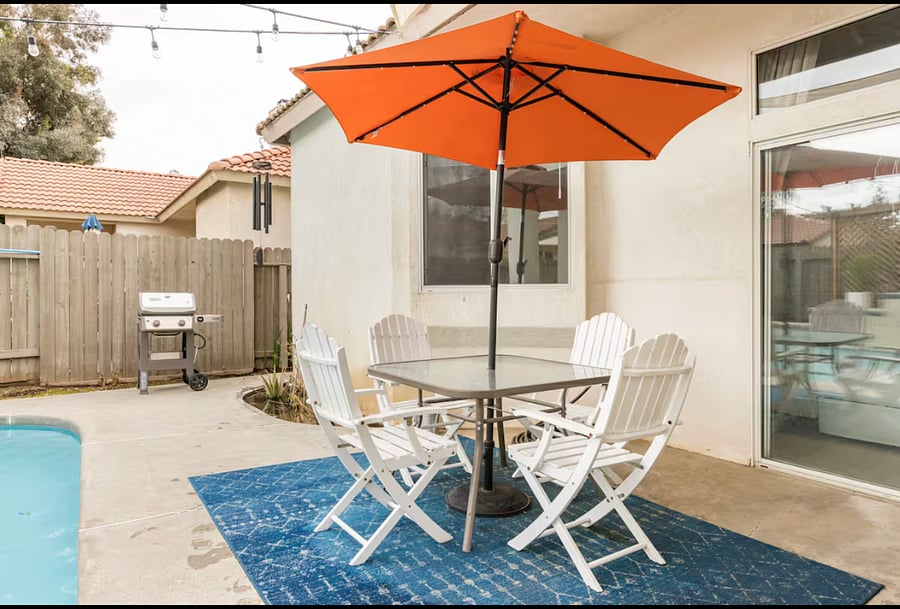 The outdoor dining area has been upgraded with a white iron table and textilene swivel chairs. The umbrella has been replaced with a sand/beige one, and the outdoor mat is refreshed annually