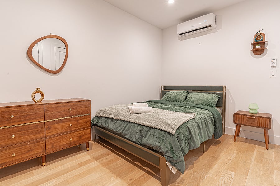 Primary bedroom setup with cozy bedding, AC, and a warm mid-century feel for restful nights.