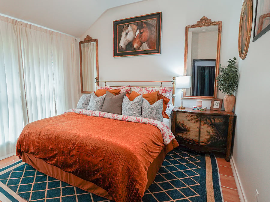 The Ralph Lauren Heritage Suite: Timeless Third Bedroom Sanctuary
Step into the third bedroom, an exquisite homage to the iconic Ralph Lauren aesthetic. Celebrated for its multi patterned elegance, layered textures, equestrian-inspired sophistication, and enduring American heritage that blends classic tailoring with cozy, inviting warmth.
This luscious bedroom retreat is richly layered in patterns and textures, centered by a vintage brass queen bed with a supremely comfortable mattress, inviting deep, restorative slumber. Flanked by a rustic wood nightstand adorned with scenic vintage motifs, the space is enveloped by a captivating gallery wall showcasing rich Mexican Art work, Texas heritage framed artwork, and US. History..
Elegant wall sconces gracefully adorn the soft Greek villa-colored walls, casting a warm, ambient glow, while flickering candles promise serene evenings of unwinding. A mid-size closet features a fabulous fabric-covered dresser for effortless organization, and an extra-large east-facing window draped in plush velvet curtains welcomes gentle morning light and golden sunset hues.
Grounded by a luxurious gold and rich navy blue rug that ties the palette in sophisticated harmony, this haven is the perfect escape after a full day's workpure layered luxury for ultimate relaxation in your curated signature Stay. 
