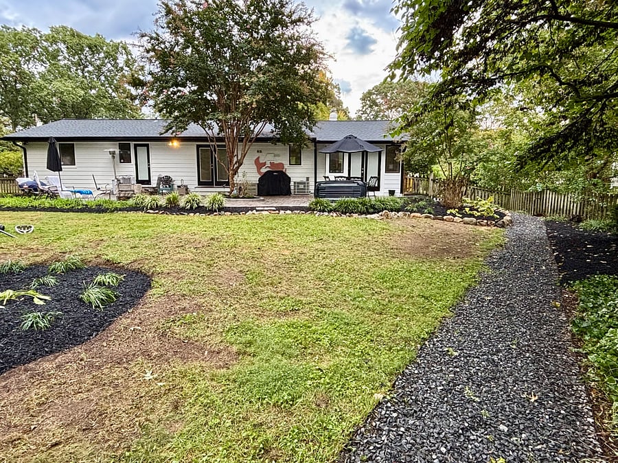 Backyard view showing private entrance door on the left, other bedroom window and fence and landscaping by outside the unit on far left and patio leading to fence gate and paved walkway to driveway on the right