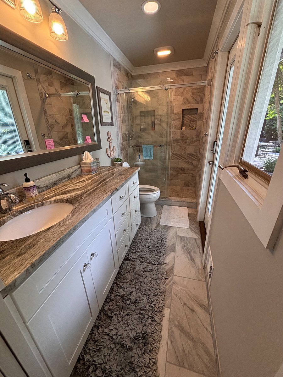 This photo shows the large extended granite vanity and many storage drawers, the casement window, pulldown screen and large walk-in shower with glass doors.