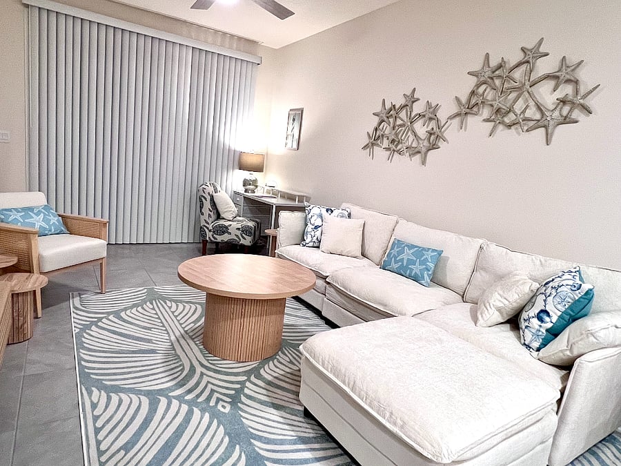 Living room with couch and dedicated workspace, ceiling fan, glass doors to outdoor patio with 2 chairs.