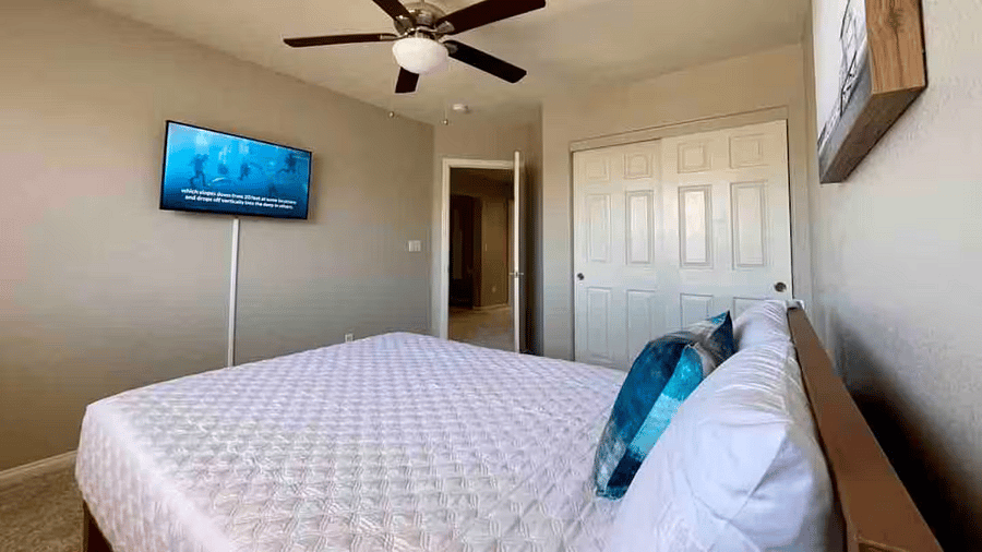 Additional view of the fourth bedroom highlighting the ceiling fan, in-room TV, and closet space.