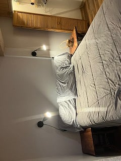 The master bedroom has a queen bed, with reading lights and side tables on either side of the bed. The room has a full closet for hanging clothes, and shelving for storage of bedding and personal items.