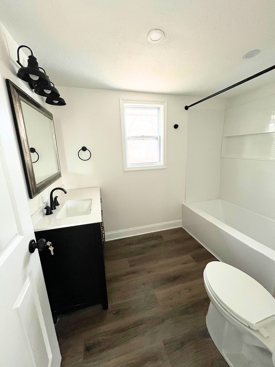 Clean Modern bathroom with bathtub, black vanity, white walls, and wood-look floor.