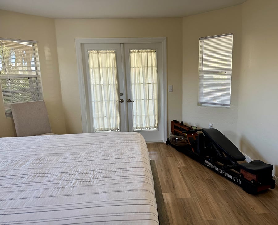 Master bedroom 1 with blinds and black out curtain on the French doors. French doors open to lanai. Exercise machine.