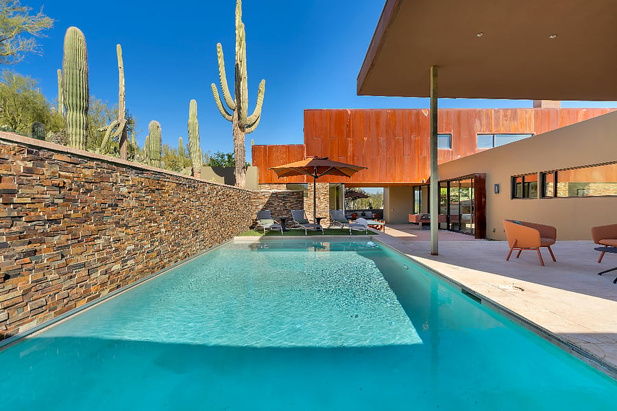 Sun-washed pool courtyard surrounded by stone walls, modern seating, and iconic desert scenery.