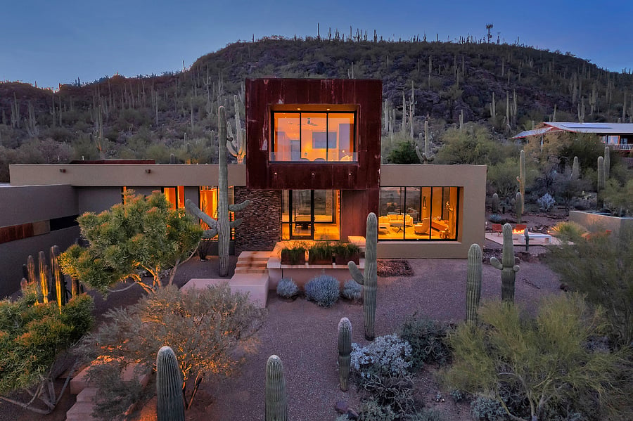 Front elevation at dusk highlighting the homes architectural lines, natural materials, and floor-to-ceiling glass.