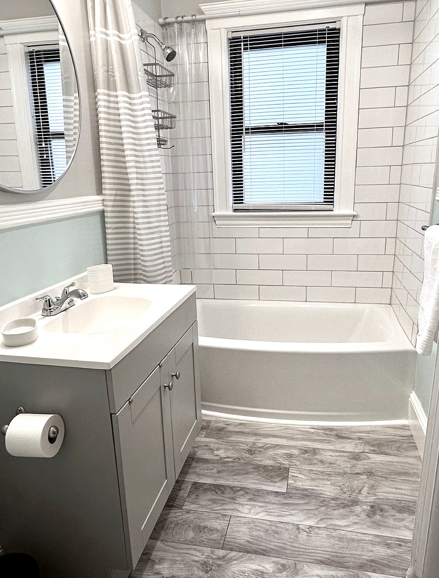 Newly renovated modern bathroom with all new fixtures, tiled shower, massage shower head. Curved tub and bowed shower curtain rail creates a spacious feel inside the shower. Toiletries and bath products provided for instant settling in.