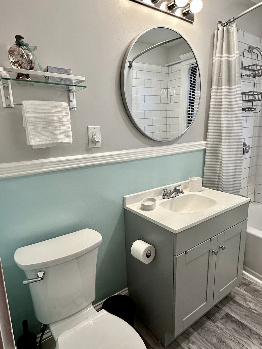 Pristine new bathroom, brightly lit with overhead and natural window light. Oversized mirror, all new fixtures and new bath rugs create a delightful and functional space