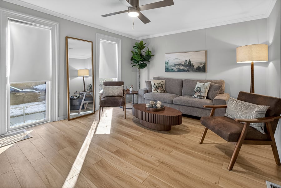 The living room features floor-to-ceiling windows that provide bright natural light, along with a sofa, two chairs, a lamp, and a securely mounted leaning full-length mirror.