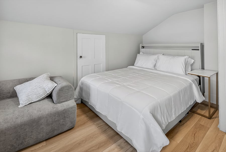 Bedroom 2 features a queen bed with an LED light frame, a side table, and a cloud sofa chair, creating a cozy and inviting space for a comfortable stay.