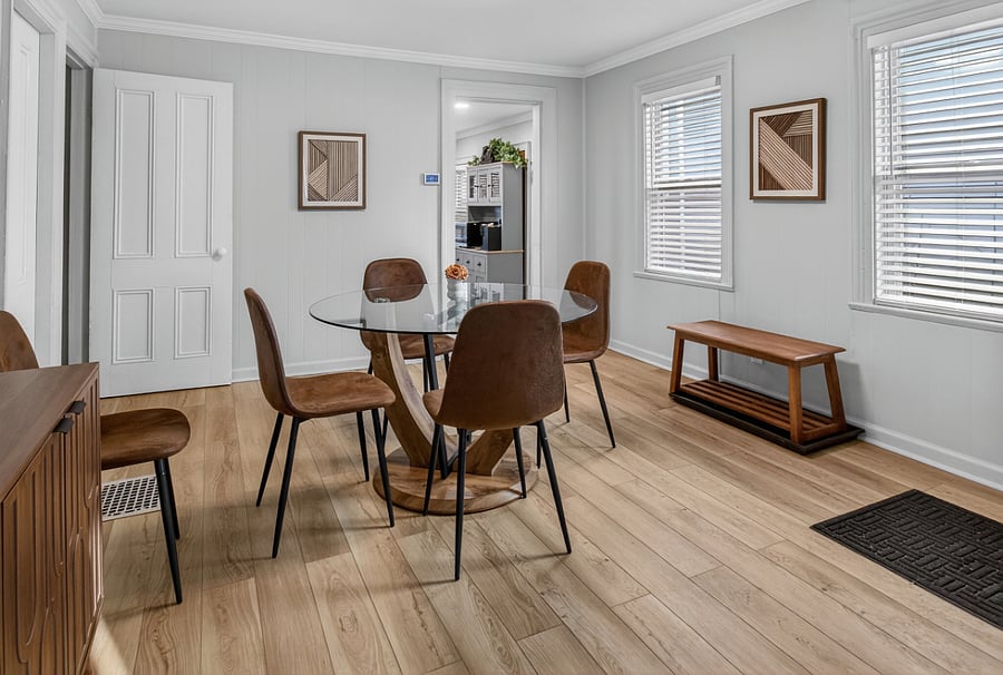 A tidy dining room with neutral walls and a Honeywell thermostat mounted neatly on the wall. Along one side near the entry, a bench sits directly on top of a large tray, creating a defined area for setting shoes on or off.
