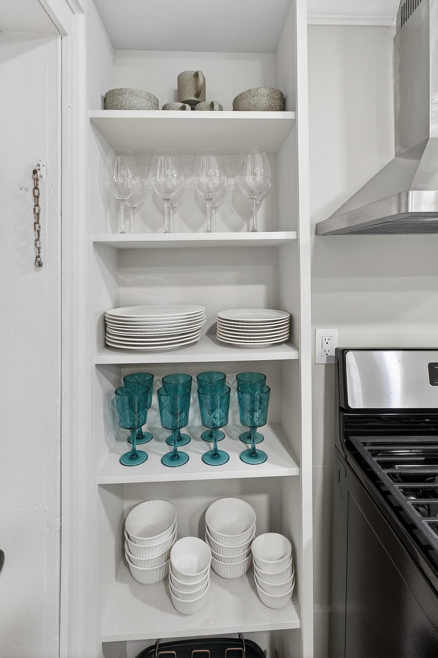 The kitchen is fully equipped with designer tableware, including wine glasses, serving sets, bowls, goblets, and a baking tray, adding a touch of elegance to every meal.