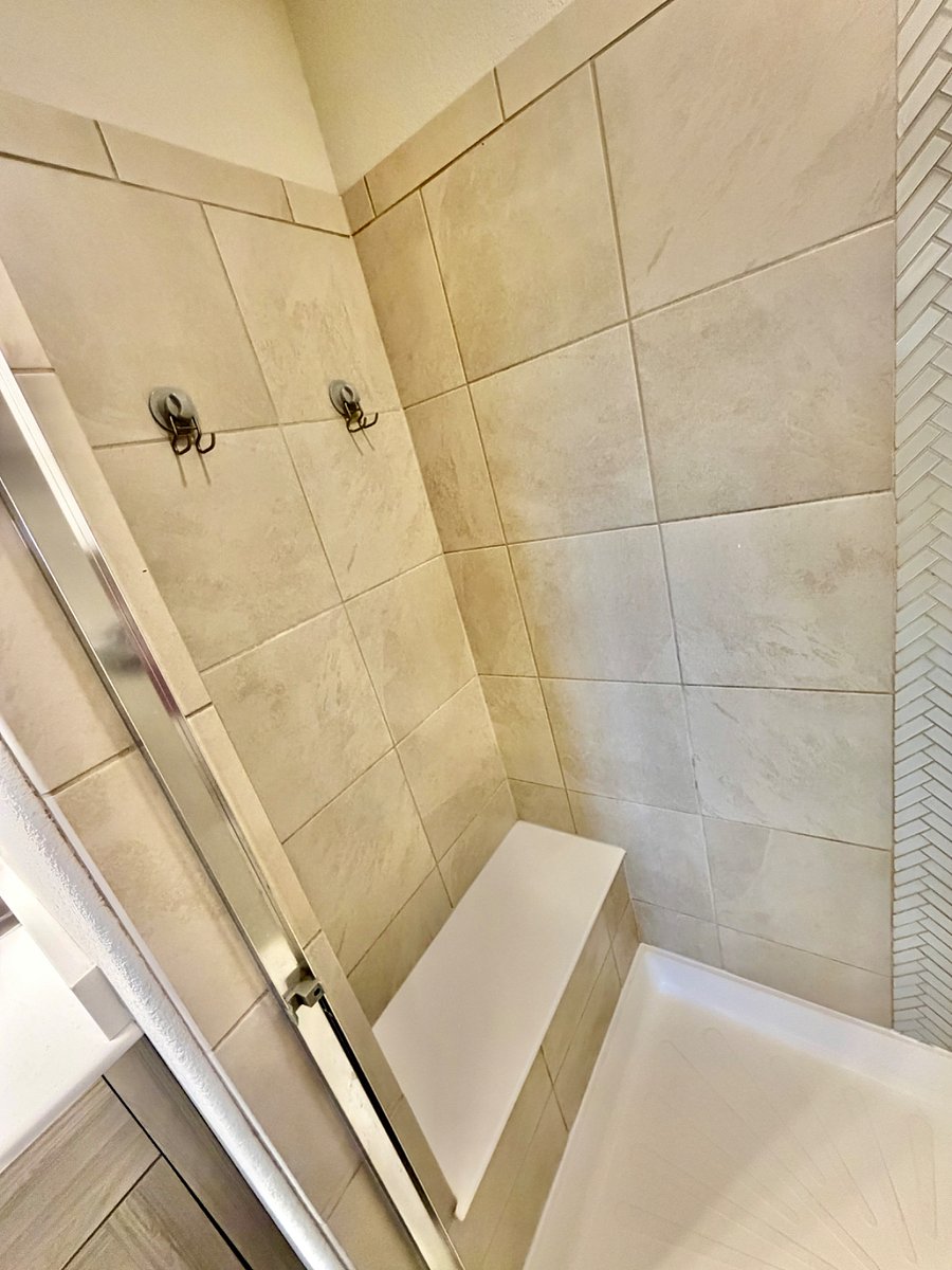 The primary bathroom features a double-sink vanity and a well-designed layout. The toilet is enclosed in its own private room, and the stand-up shower includes a built-in bench for added comfort and convenience.