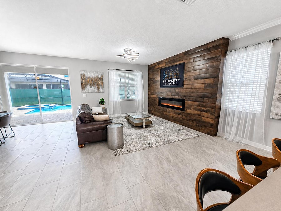 Spacious living room with tiled floors, large windows, and sliding doors opening to a pool patio plus an accent fireplace wal