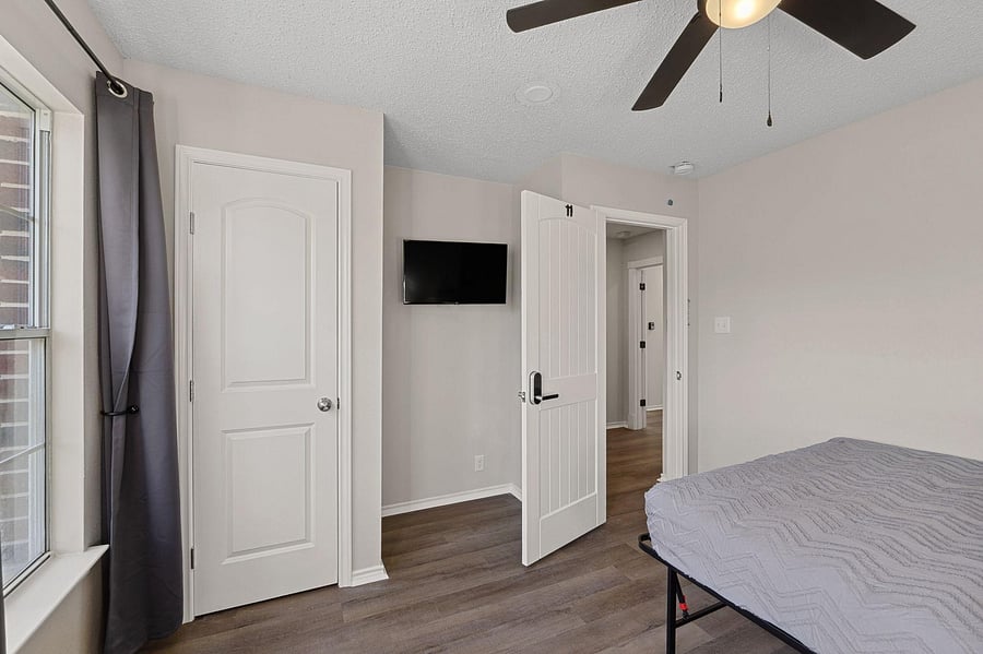 Bedroom with comfortable bed, a mini fridge, a TV, and a work desk. A mini closet & a ceiling fan.