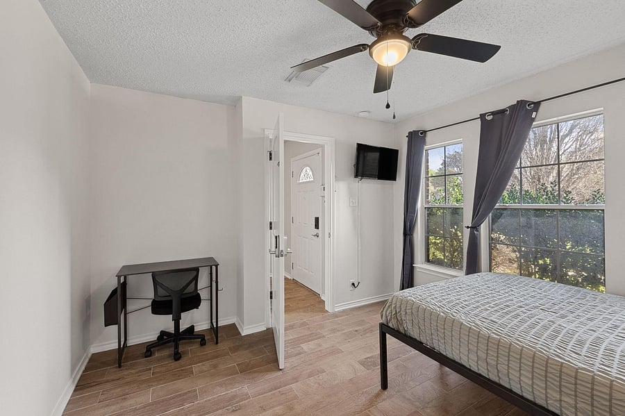 Bedroom with comfortable bed, a mini fridge, a TV, and a work desk. A closet & a ceiling fan.