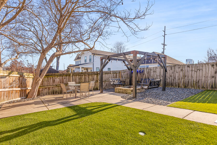 Fully fenced-in backyard with outdoor seating, swings, fire pit, turf and a grill.
