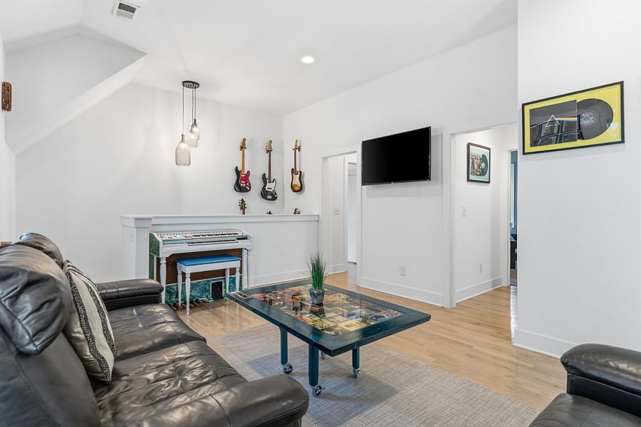 Second living room area on the second floor with comfortable seating, smart TV, piano and guitars.