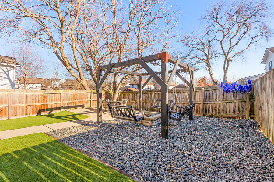 Fully fenced-in backyard with outdoor seating, swings, fire pit, turf and a grill.