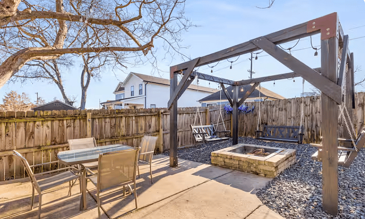 Fully fenced-in backyard with outdoor seating, swings, fire pit, turf and a grill.