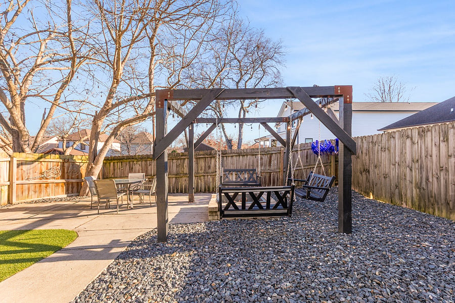 Fully fenced-in backyard with outdoor seating, swings, fire pit, turf and a grill.