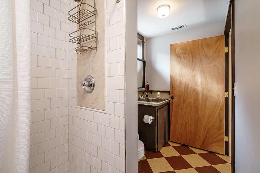 Apartment bathroom with large, tiled shower, toilet, storage and sink/vanity with transom window