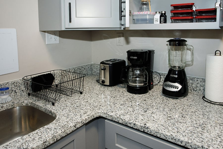A fully stocked kitchen is equipped with all the essentials needed for meal preparation and entertaining. Modern Grey cabinets house a variety of cookware, such as pots, pans, and baking dishes, along with a full range of utensils like a set of 4 plates, quarter plates, cups, wine glasses, mugs, including knives, spatulas, oil bottles storage containers and measuring cups. Additionally, small appliances like a toaster, blender, and coffee maker are readily available, ensuring comfort and versatility for all cooking tasks. Dishwashing liquid along with a dish drainer rack are provided for added convenience. Luxurious Stainless-Steel Microwave, Range and a refrigerator are installed in the kitchen. 