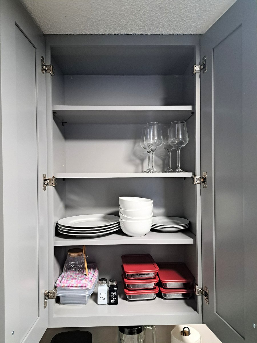 A fully stocked kitchen is equipped with all the essentials needed for meal preparation and entertaining. Modern Grey cabinets house a variety of cookware, such as pots, pans, and baking dishes, along with a full range of utensils like a set of 4 plates, quarter plates, cups, wine glasses, mugs, including knives, spatulas, oil bottles storage containers and measuring cups. Additionally, small appliances like a toaster, blender, and coffee maker are readily available, ensuring comfort and versatility for all cooking tasks. Dishwashing liquid along with a dish drainer rack are provided for added convenience. Luxurious Stainless-Steel Microwave, Range and a refrigerator are installed in the kitchen. 