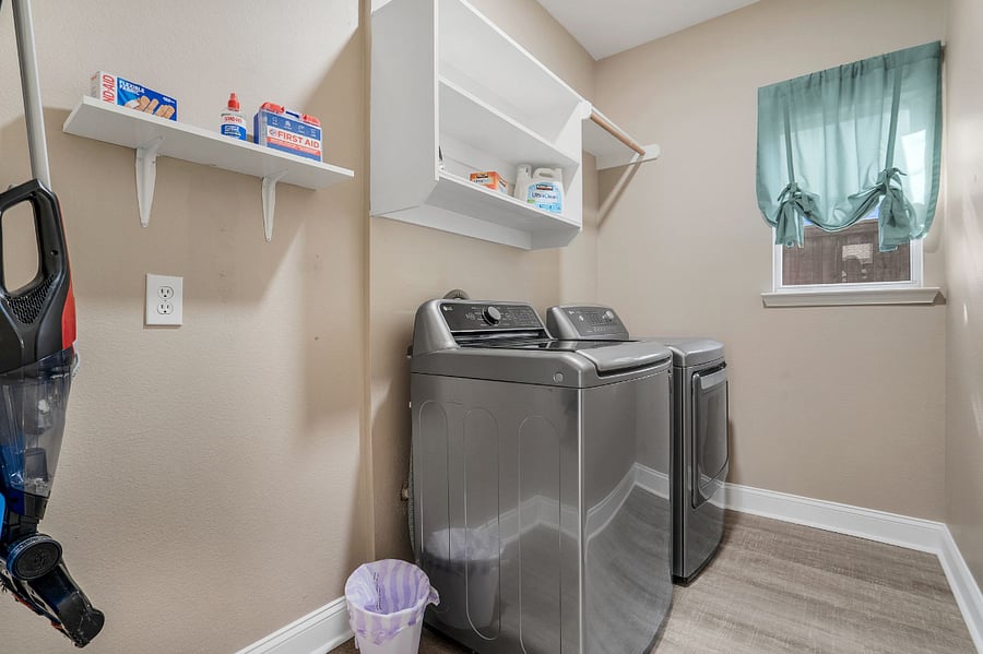 Washer and dryer, with drying rack, vac and cleaning supplies in laundry room near kitchen