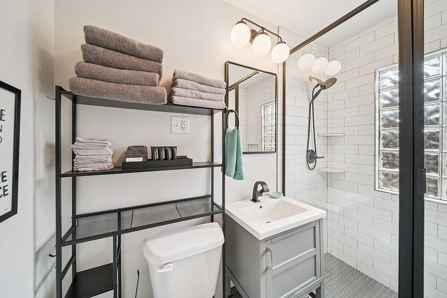 A second view of the updated main bathroom showcases the spacious walk-in tiled shower with a handheld shower head, designed for comfort and convenience. Guests are provided with bath linens and a starter kit of toiletries upon arrival. The bathroom also includes a linen closet for convenient storage of towels and extra linens, although it is not visible in this photo.