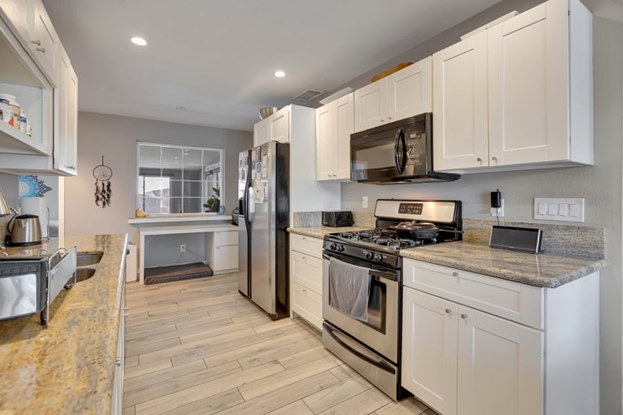 Light-filled kitchen w/granite countertops, stainless steel appliances, and white cabinetry