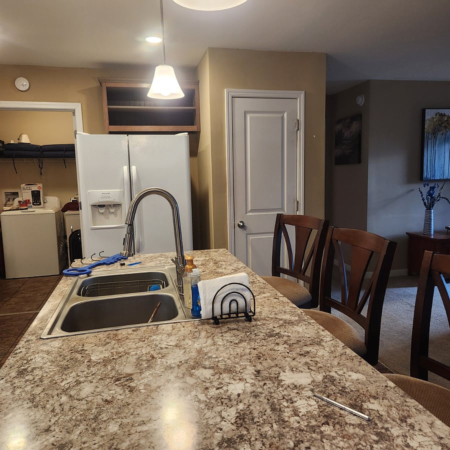 Kitchen island view with sink, 3 barstools, views of pantry, refrigerator and laundry room.