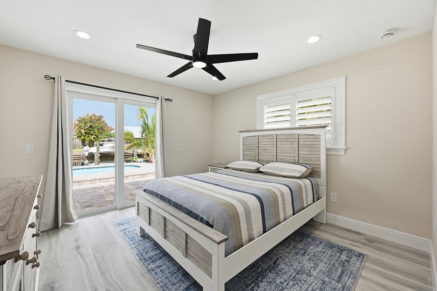 View of third bedroom with queen bed looking out sliding glass door leading to pool deck. 