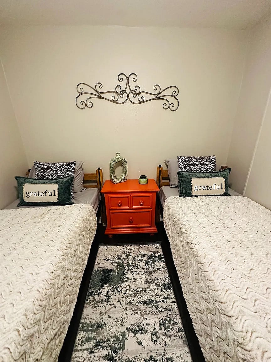 Perfect for travel pairs or friends! This versatile room features two comfortable twin beds and charming "Grateful" decor. Includes a shared nightstand and plenty of natural light for a bright, welcoming atmosphere.
