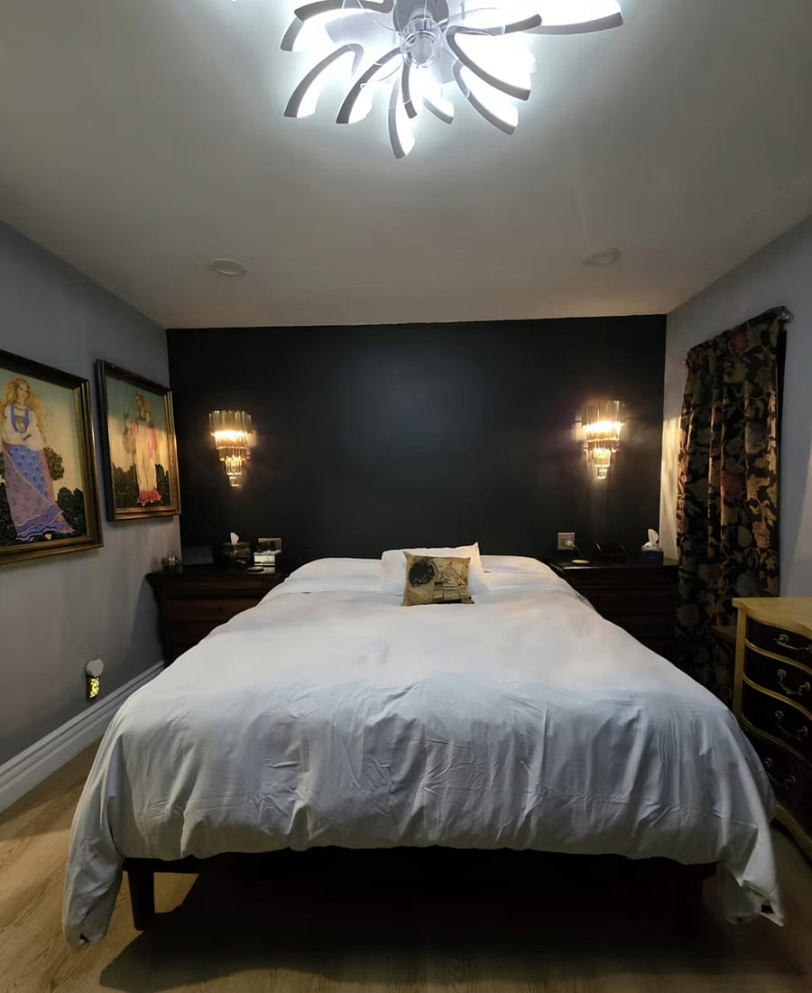Executive primary suite featuring a luxurious California King bed, Hollywood Regency wall sconces, chandelier ceiling fan, and spa-style ensuite bathroom with bidet. Bedside outlets for device charging.
