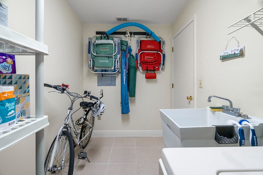 Laundry room containing two bicycles, beach, chairs, beach, umbrellas, and other extras for the area.