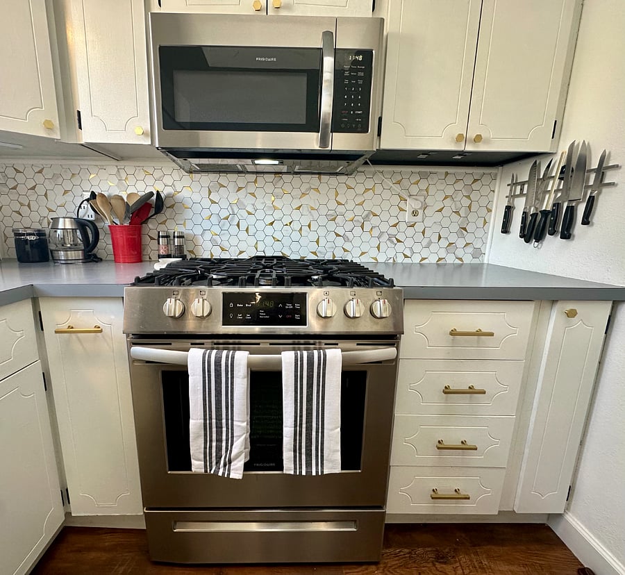 Four-burner gas stove with oven and microwave, large assortment of high-quality knives, cooking utensils, and hot water/tea kettle.