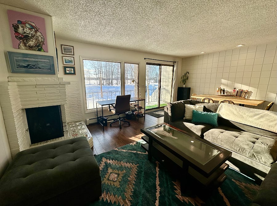 Natural light pouring into the multi-purpose, light-filled space with desk, sectional couch, and dining table for four.