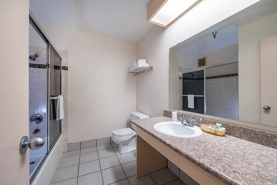 Clean and spacious private bathroom featuring a tub/shower combination, large vanity with granite countertop, bright lighting, fresh towels, and essential toiletries. Designed for comfort and convenience during both short and extended stays.