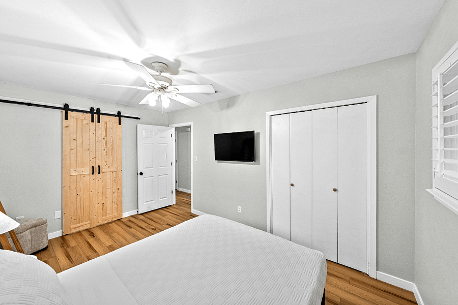 Primary bedroom shot with queen bed, closet and mounted smart TV.