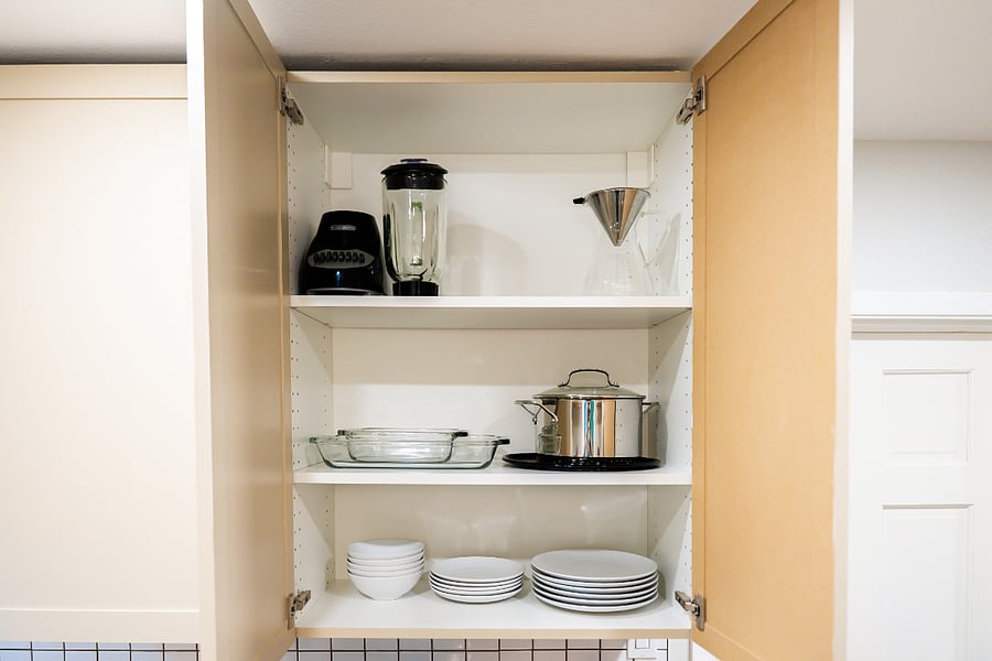 Kitchen cabinet with blender, drip coffee maker, dinnerware and cookware.